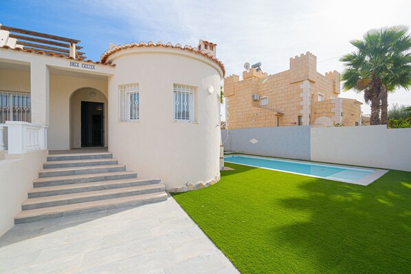 A building with a sign reading "HOLA CASTILLA" and a pool area with artificial grass.