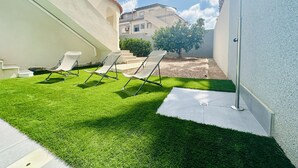 Une cour avec une pelouse artificielle, un mur blanc et un bâtiment en arrière-plan.