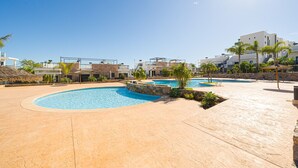 Un espace piscine comprenant plusieurs bassins, des allées pavées et des bâtiments modernes en arrière-plan.