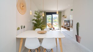 Un espace de salle à manger moderne avec une table blanche, des chaises en bois, des luminaires suspendus et des plantes en pot.