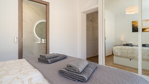 A modern hotel room with a large bed, a bathroom with a mirror and sink, and a separate bedroom with a bed and nightstand.