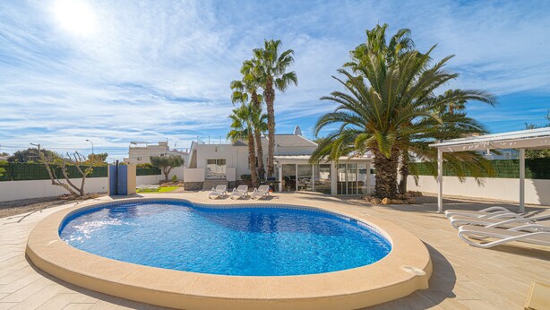 A swimming pool with lounge chairs, palm trees, and a modern building in the background.