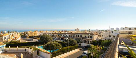 A residential area with a red car parked in a driveway, a swimming pool, and a view of the sea in the background.