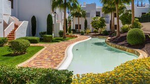 A pool area with a curved pathway, palm trees, and neatly trimmed bushes. - Casa Musica (Mar de Pulpi) (San Juan de los terreros)