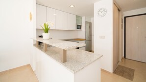 A modern kitchen with white cabinetry, a microwave, a clock, and a small potted plant. - Sole Mio (Terrazas de Campoamor) (Orihuela Costa)