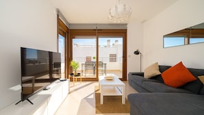 A modern living room with a flat-screen TV, a grey sofa with orange cushions, a white coffee table, and a balcony with a dining area. - Sole Mio (Terrazas de Campoamor) (Orihuela Costa)