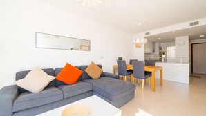 A modern living room with a grey sectional sofa, a white coffee table, and a dining area with a wooden table and chairs. - Sole Mio (Terrazas de Campoamor) (Orihuela Costa)