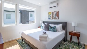 A modern bedroom with a large bed, two windows, a ceiling fan, and artwork on the wall. - Basecamp - a PMI Scenic City Vacation Rental (Chattanooga)