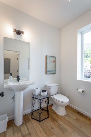 A modern bathroom with a white sink, toilet, and a small table with a bottle of hand soap. - Basecamp - a PMI Scenic City Vacation Rental (Chattanooga)
