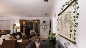 A living room with a brown sofa, a black armchair, a coffee table, and a TV. There is a world map on the wall and a plant on the floor. - Boho Gator Lux 2 Ft. Myers (Lehigh Acres)