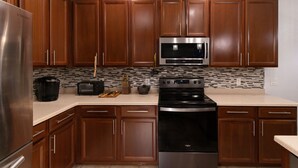 A modern kitchen with wooden cabinets, a stainless steel refrigerator, a microwave, and a stove. - Boho Gator Lux 2 Ft. Myers (Lehigh Acres)