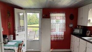 A kitchen with a red wall, white cabinets, a dining table with chairs, a window with curtains, and a door leading outside.