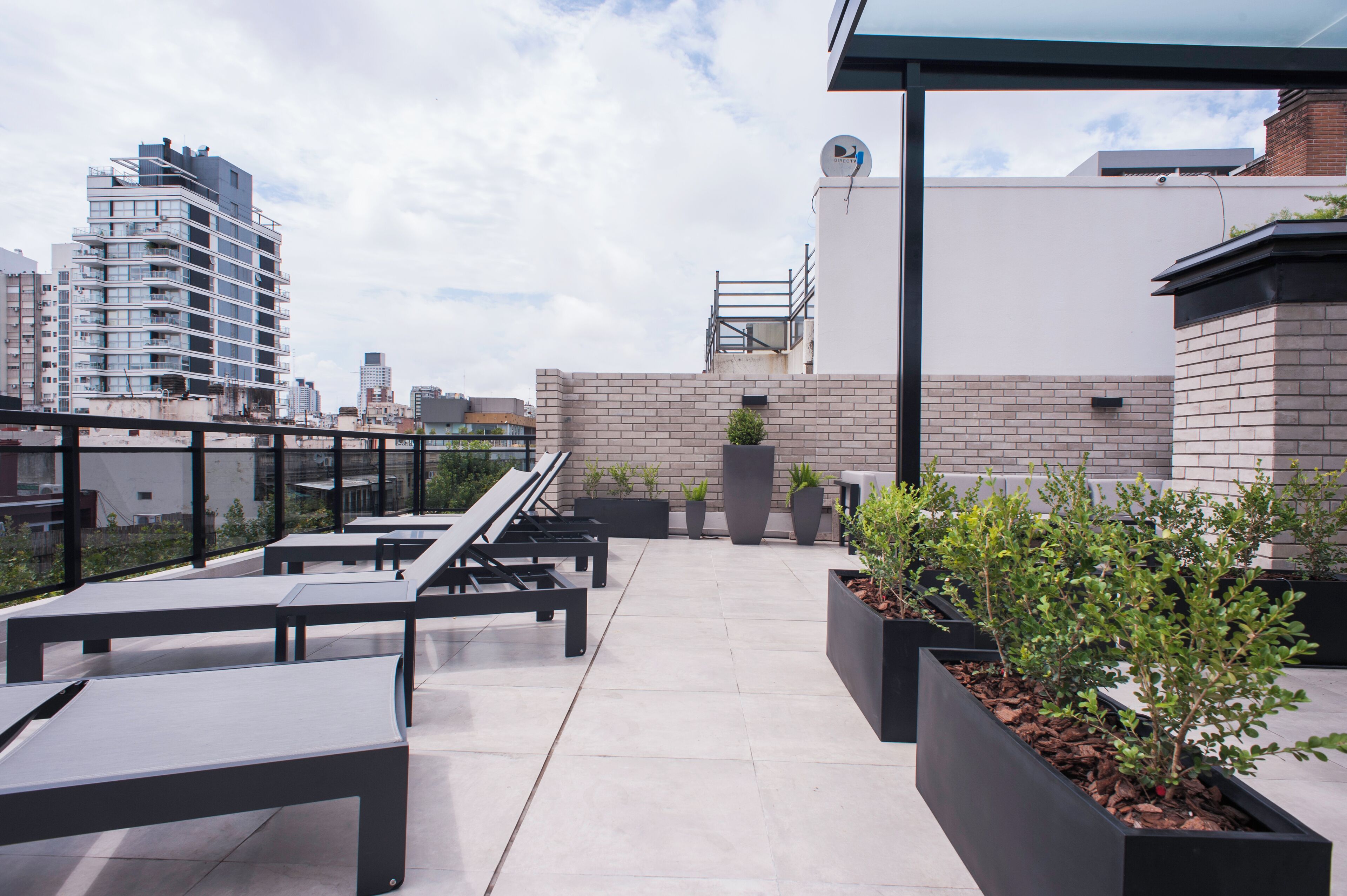 A rooftop terrace with outdoor seating, potted plants, and a view of the city skyline.