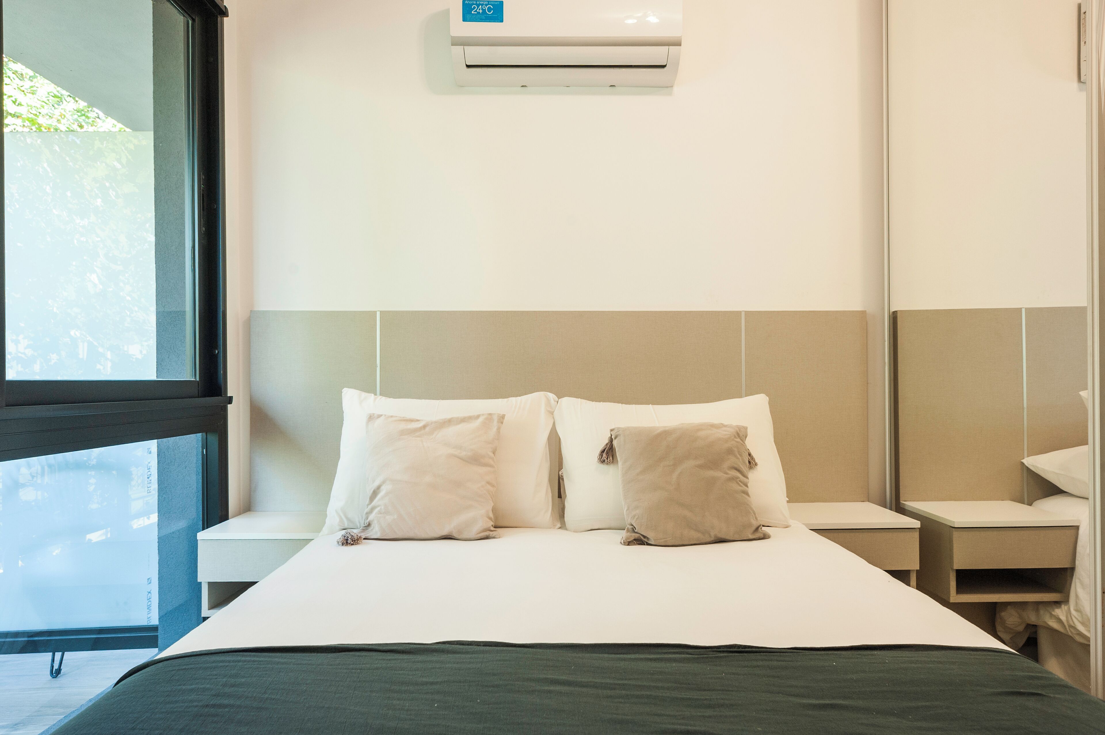 Een hotelkamer met een bed, twee nachtkastjes, een raam en een airconditioning.