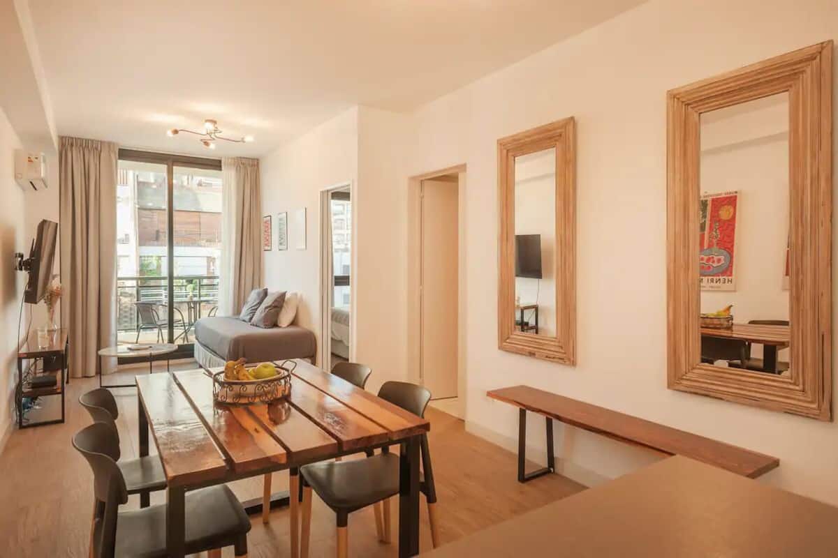 A modern living room with a sofa, a dining table with chairs, and a large mirror on the wall.