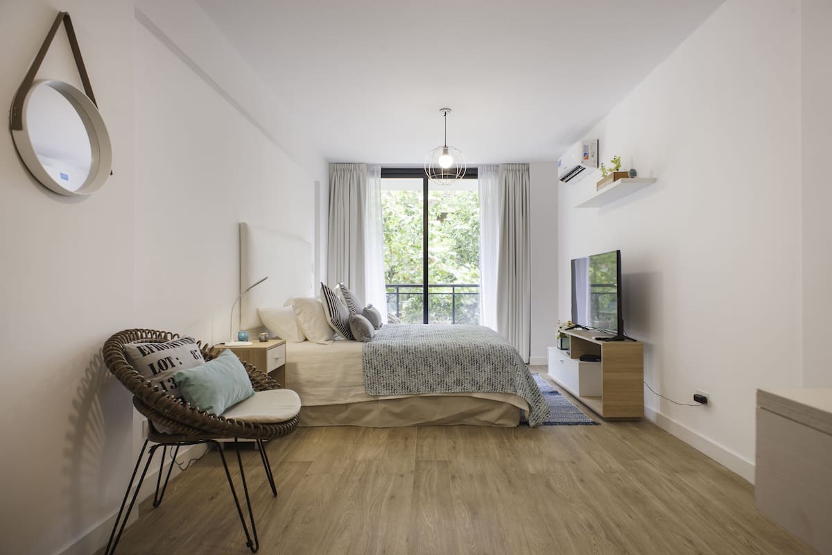 A modern bedroom with a bed, a chair, a TV, and a window with curtains.