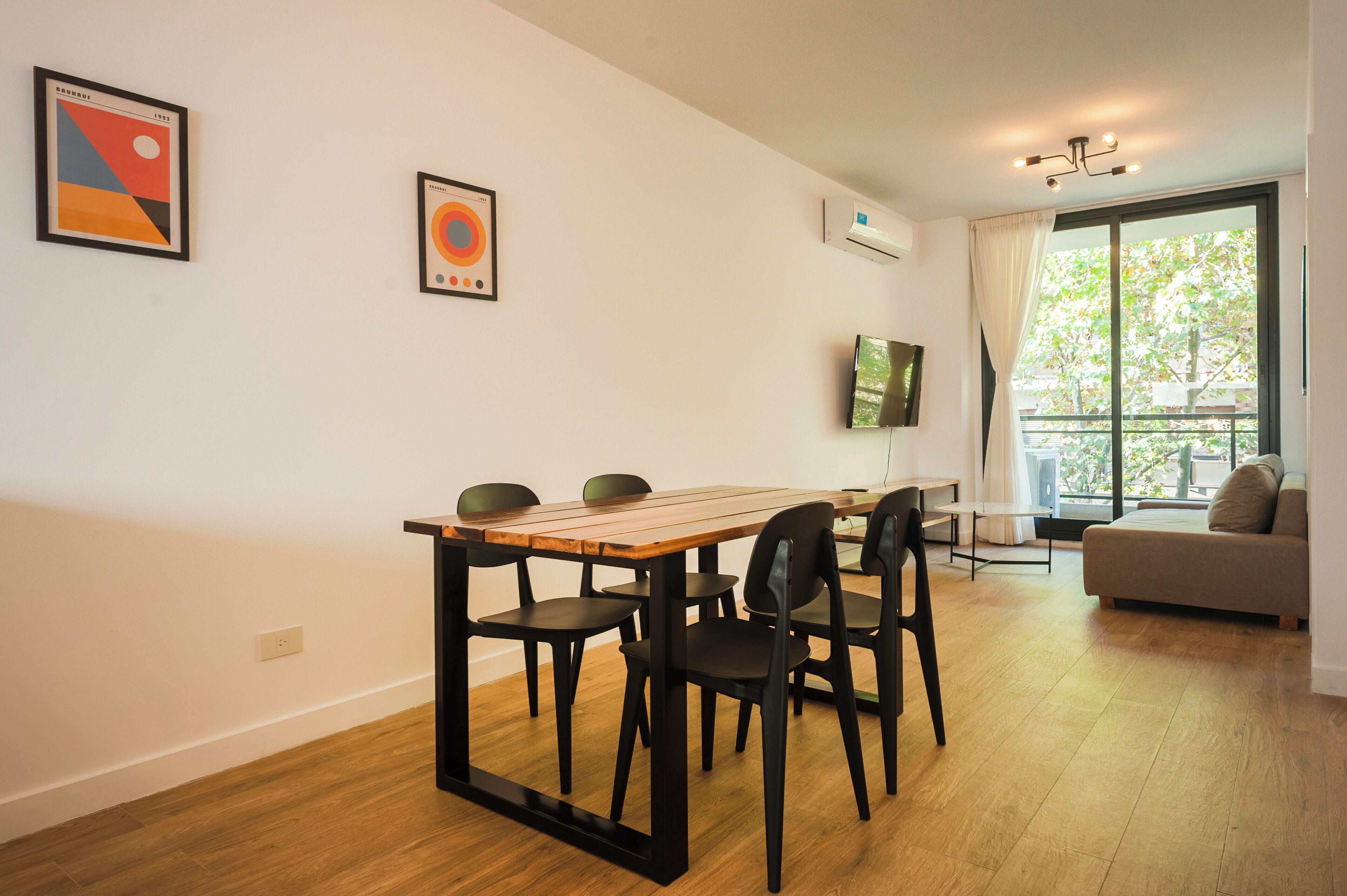 A modern living room with a dining table, chairs, a sofa, and artwork on the walls.