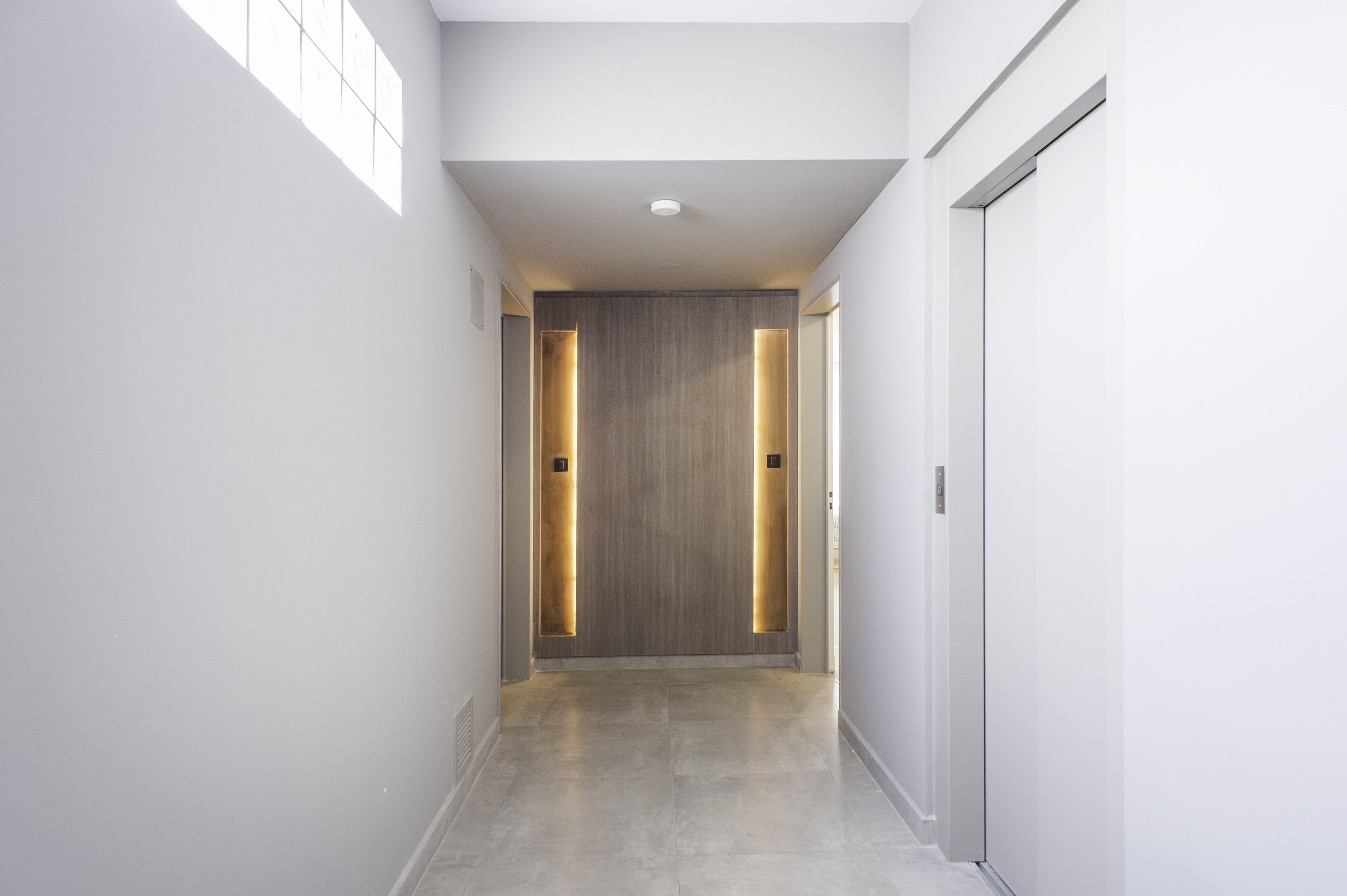 A modern hallway with a wooden door and a light fixture on the wall.