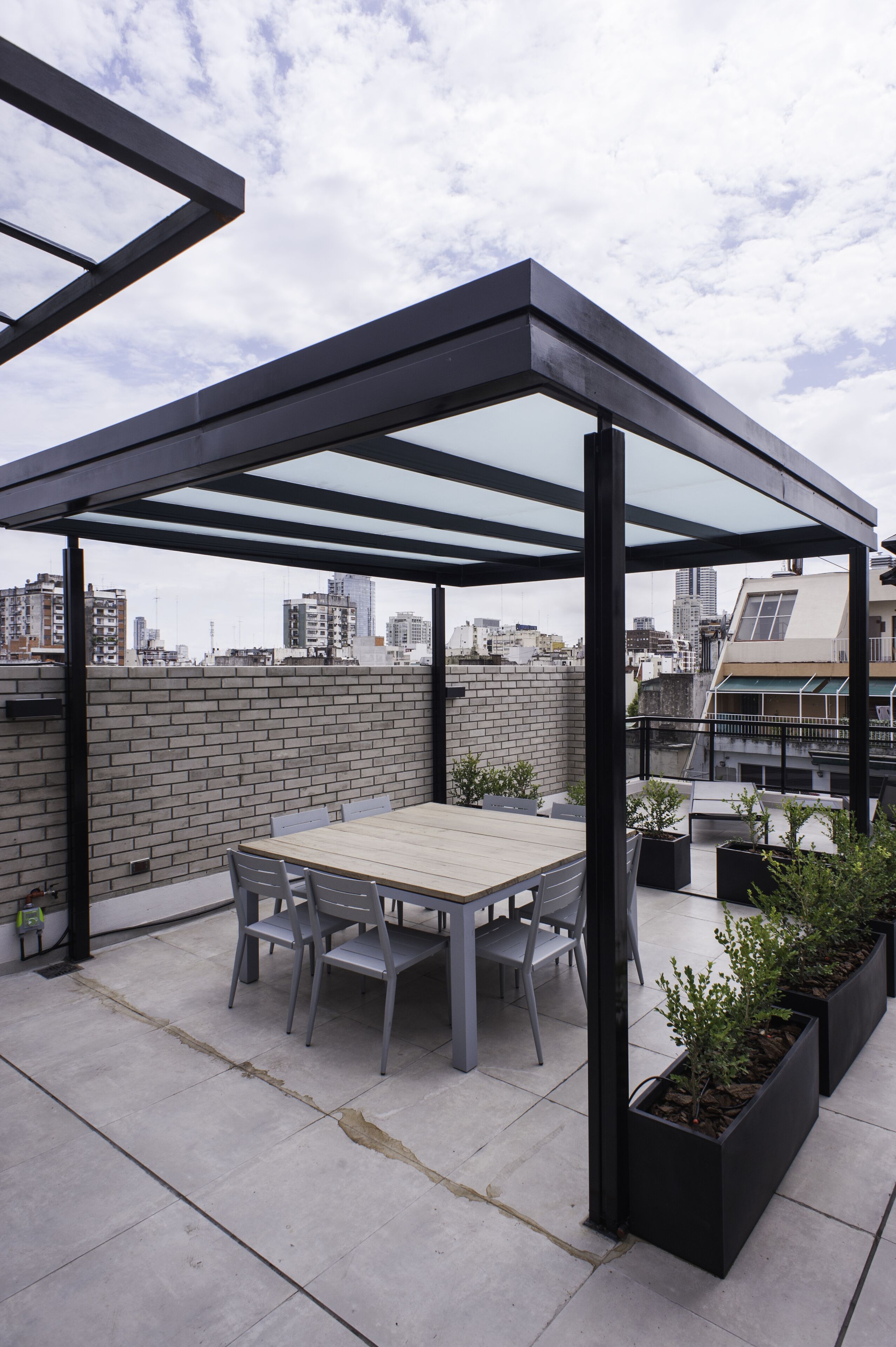 A rooftop patio with a table and chairs, a glass enclosure, and potted plants.