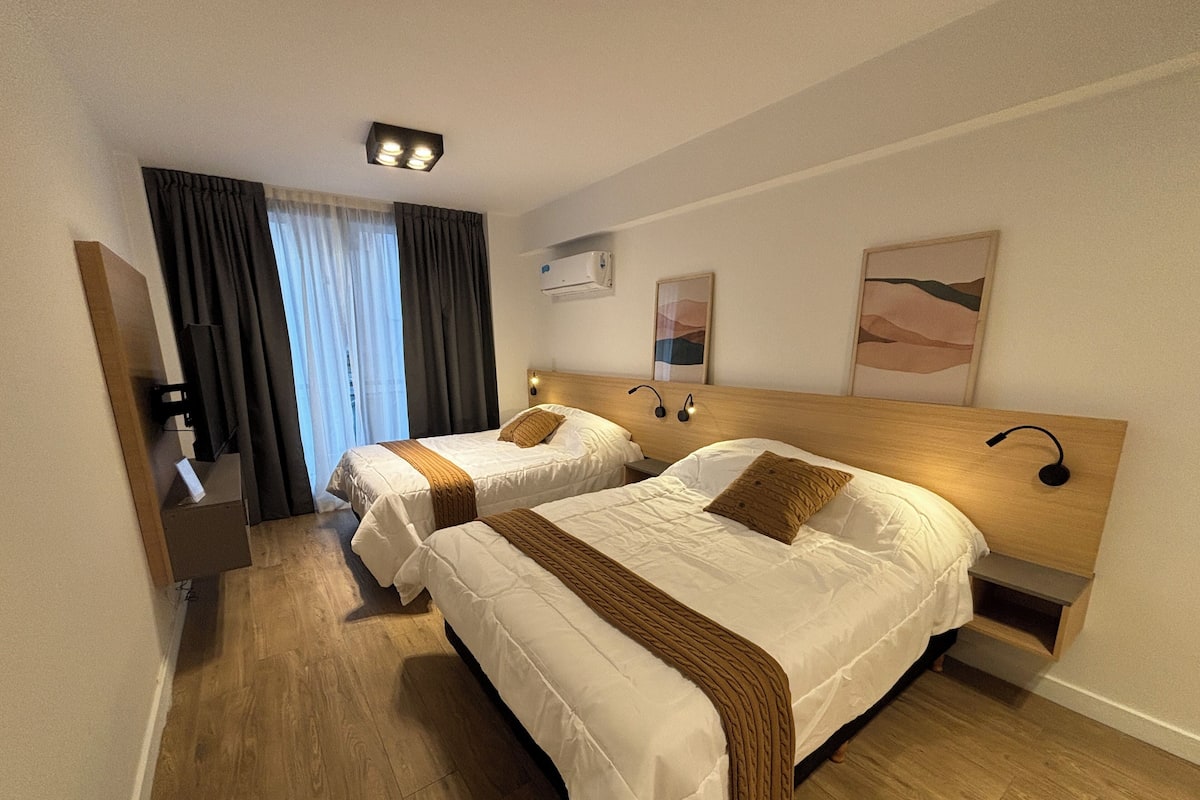 A hotel room with two beds, a nightstand, a desk, and a window with curtains.
