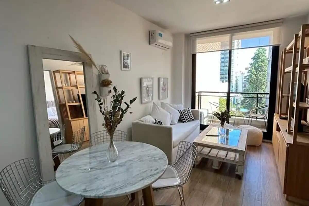 A modern living room with a marble table, white sofa, and a balcony with a view of the city.