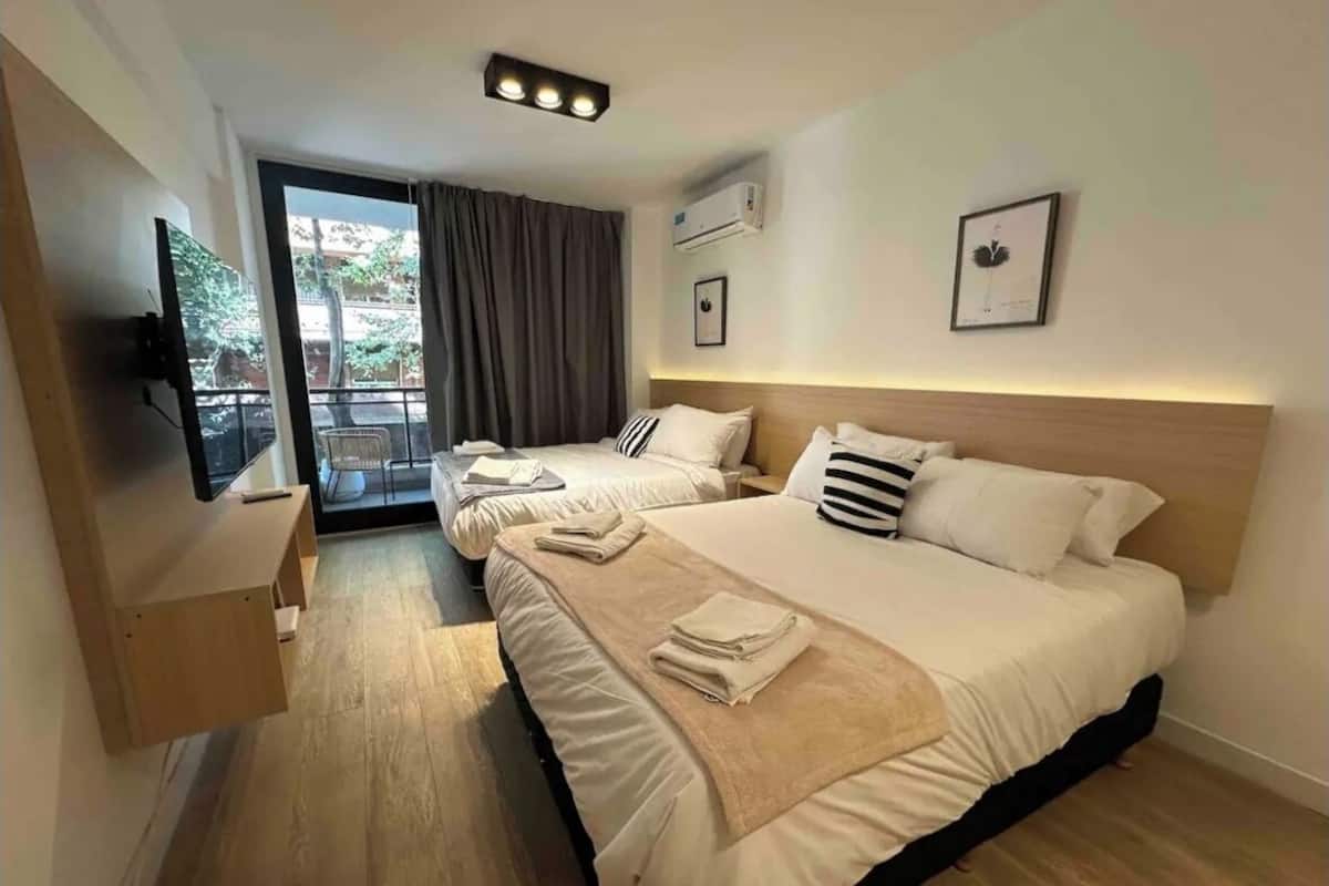 A hotel room with a large bed, a TV, a balcony, and a view of the outdoors.