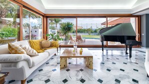A spacious living room with a grand piano, a white sofa with yellow cushions, and a large glass door leading to an outdoor pool area. - Magic house with private pool and games (San Bartolomé de Tirajana)