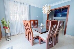 Un comedor con mesa de vidrio, sillas de madera, lámpara colgante y planta en maceta.