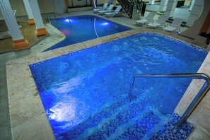 Una piscina interior con agua cristalina, borde de azulejos y una escalera de metal.