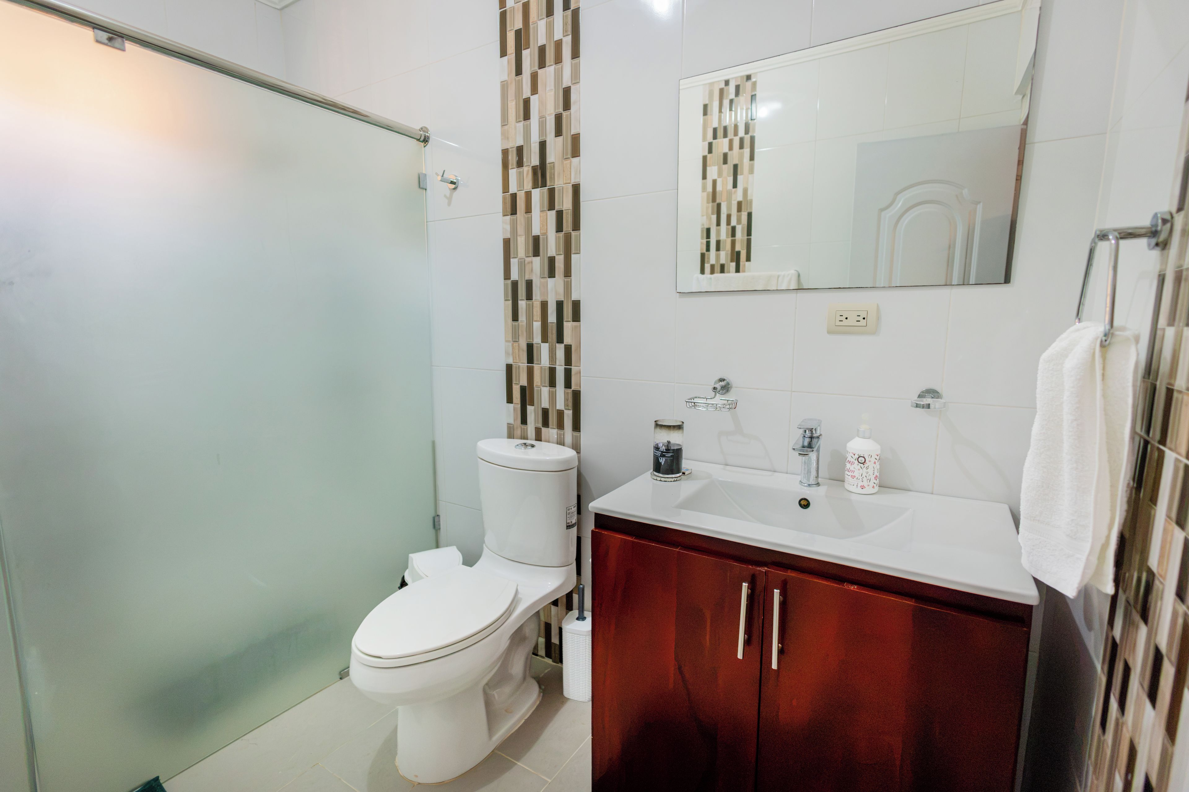 Un baño con inodoro, lavamanos, espejo y zona de ducha.
