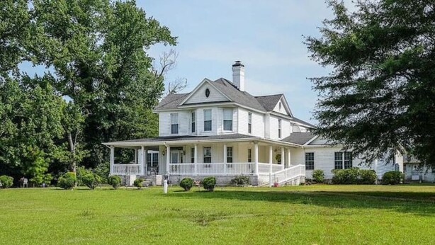A large, two-story house with a wrap-around porch, surrounded by a well-maintained lawn and trees.