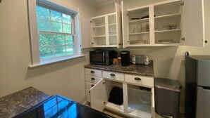 A compact kitchen with white cabinets, a microwave, a coffee maker, and a refrigerator.