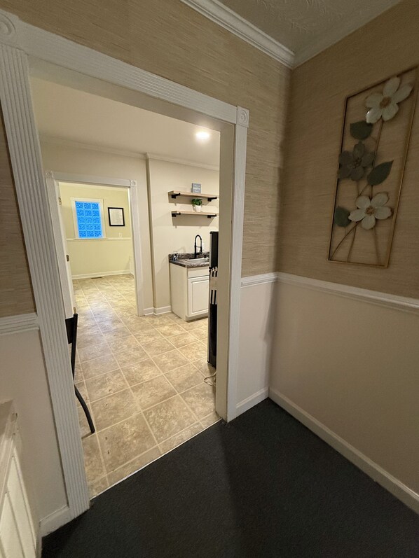 Un corridoio con un'area cucina sullo sfondo, una porta che conduce in un'altra stanza e un muro decorato con motivi floreali.