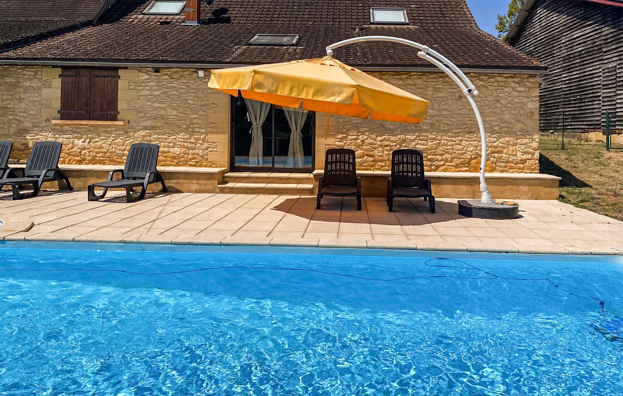 A swimming pool with a patio area, including a covered seating area with chairs and an umbrella.
