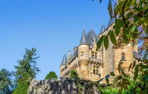A historic castle with multiple towers and a prominent entrance, surrounded by lush greenery.