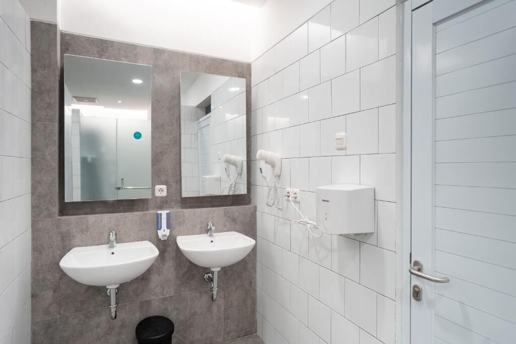 A modern bathroom with two sinks, a mirror, and a hairdryer on the wall.