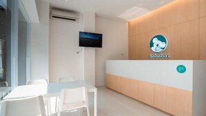 A reception area with a wooden reception desk, a mounted TV, and a white table with chairs. - Bobopod Kebayoran Baru Jakarta (Jakarta)