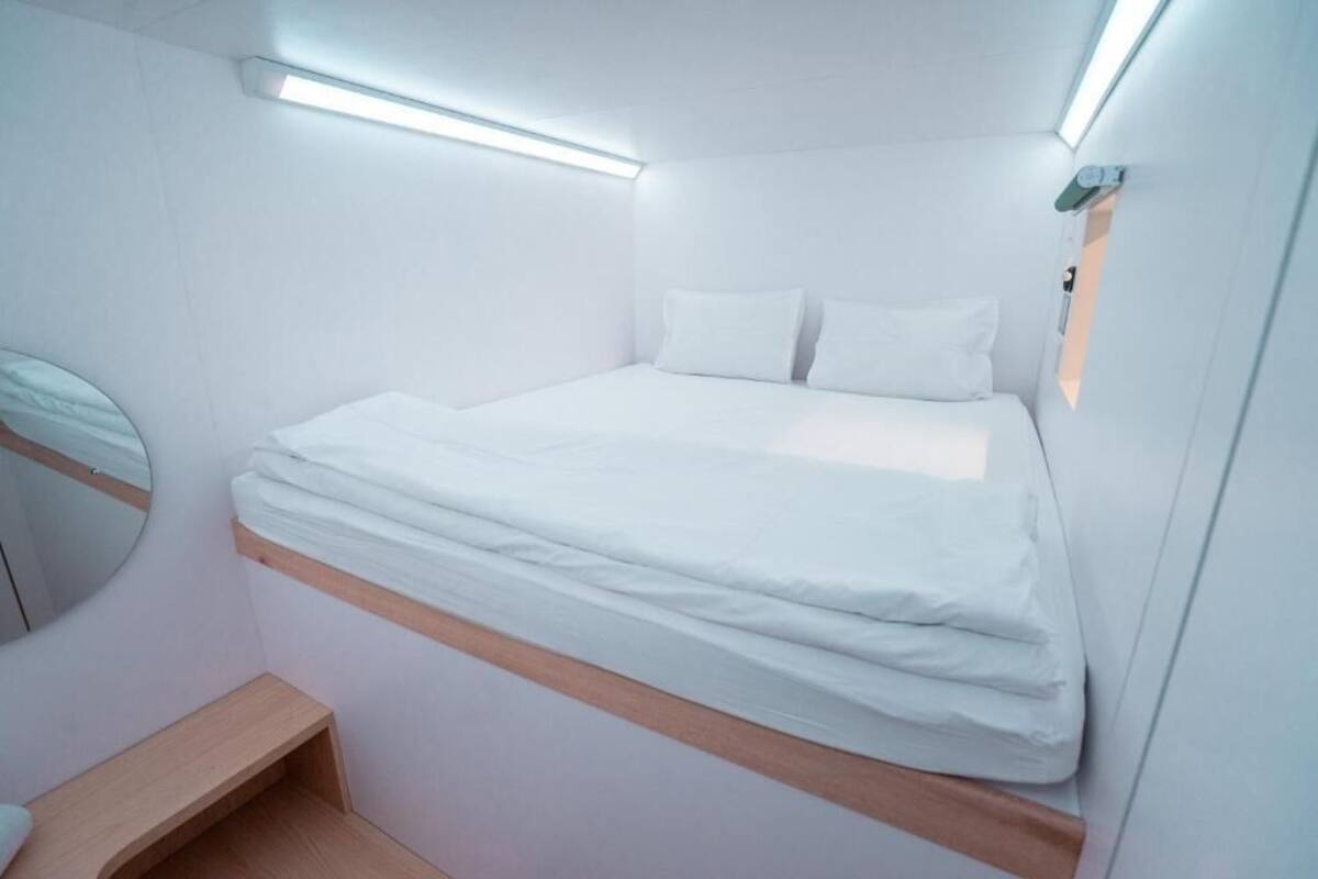 A compact, modern room with a bed, a small wooden bench, and a mirror.