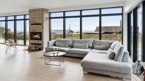 A modern living room with a fireplace, a sectional sofa, a round coffee table, and large windows offering a view of the sea.