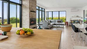 A modern living room with a fireplace, large windows, and a dining area with a fruit bowl.