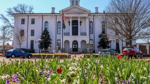 A white building with a clock tower, a flag, and a garden with tulips. - Hotty Toddy Condo at 514 by Apex Short Term Stays (Oxford)