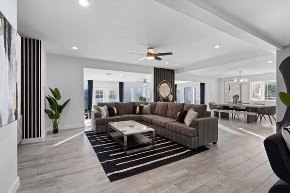 A modern living room with a sectional sofa, a coffee table, and a dining area with a large table and chairs.