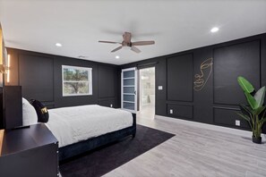 A modern bedroom with a bed, a ceiling fan, a window, and a plant.