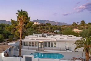 Una casa moderna con piscina, rodeada de montañas y palmeras.