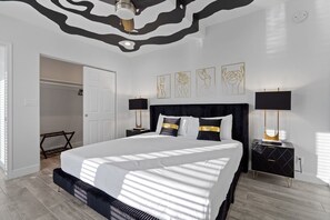 Un dormitorio moderno con una cama grande, dos mesitas de noche con lámparas, un armario y una obra de arte abstracta en la pared.
