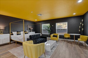 Un dormitorio moderno con cama con dosel, un sofá, sillas amarillas y una pequeña mesa redonda.