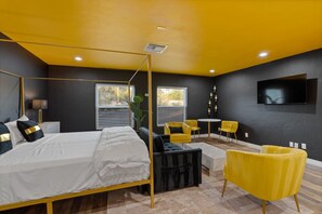 Un dormitorio moderno con una cama con dosel, una zona de estar con sillas amarillas y un televisor de pantalla plana montado en la pared.