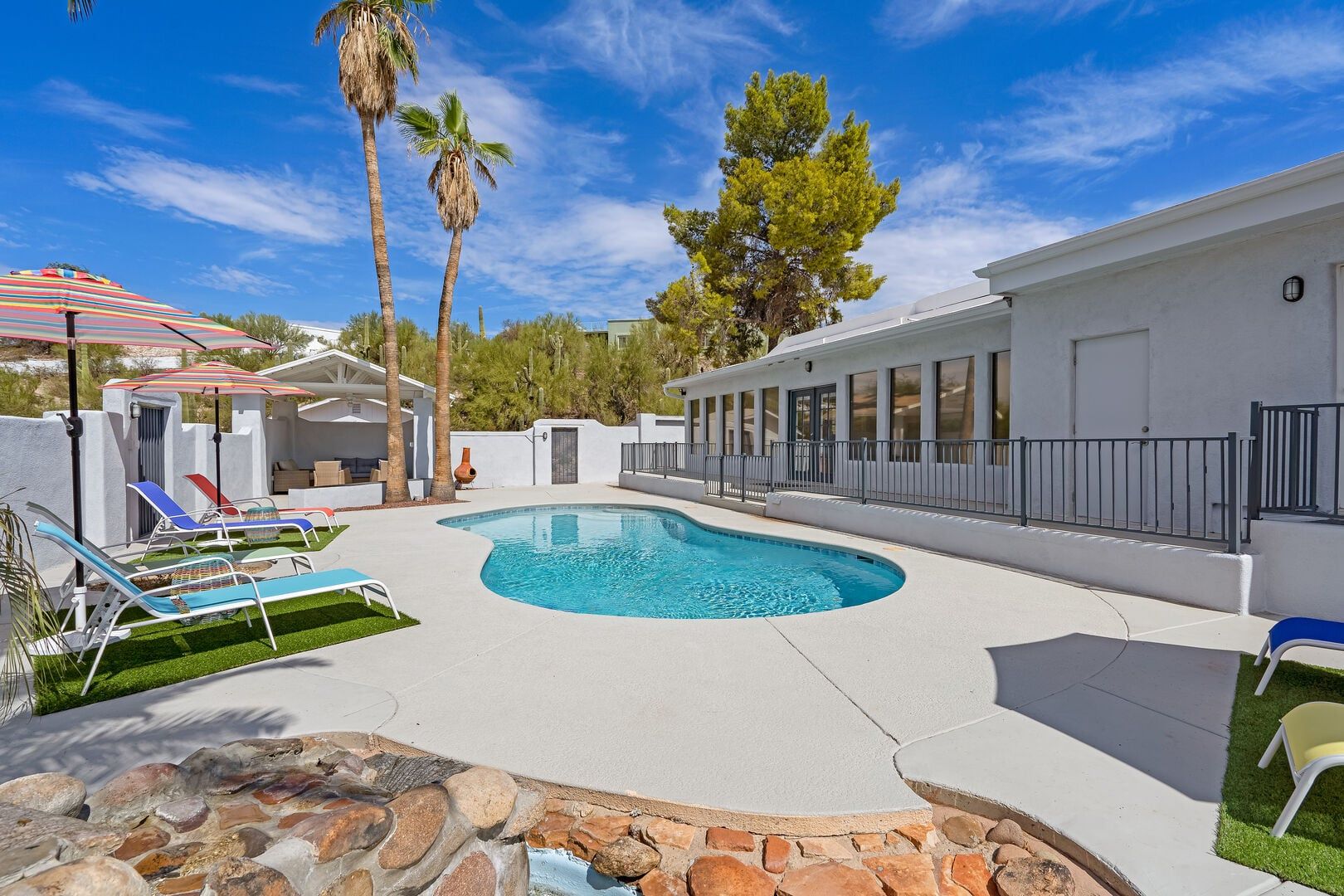 A swimming pool with lounge chairs, a stone border, and a white building with windows.