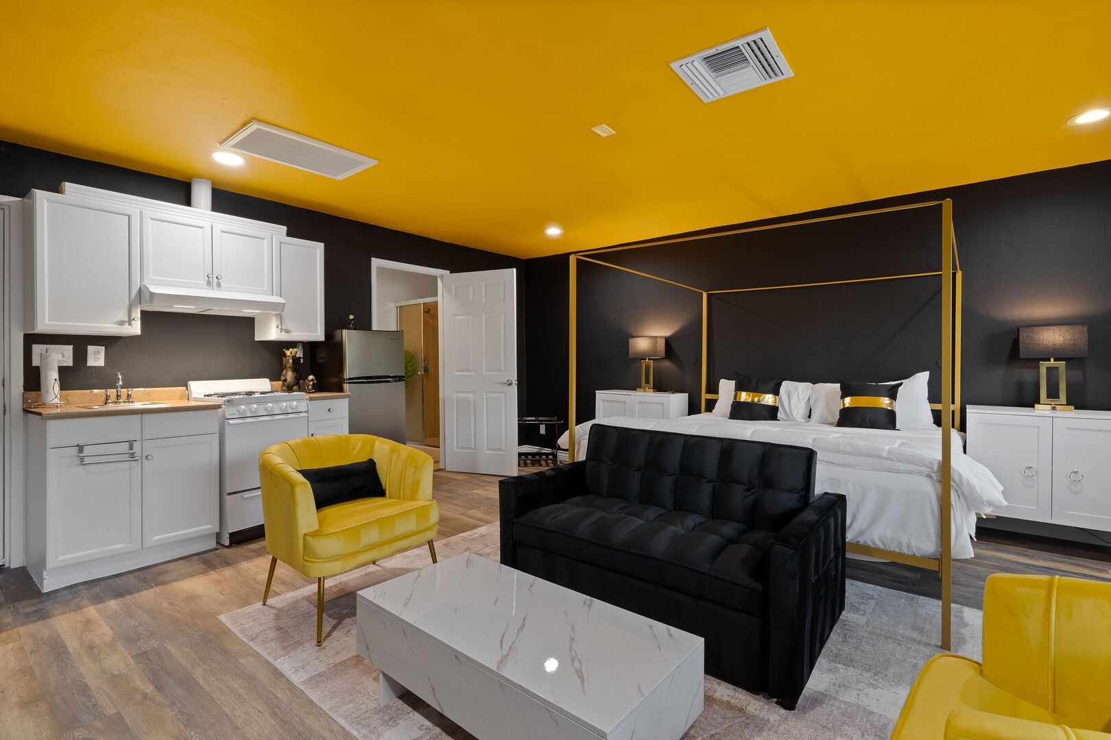 Ein modernes Hotelzimmer mit Himmelbett, separatem Essbereich mit Herd und einem gelben Sessel.