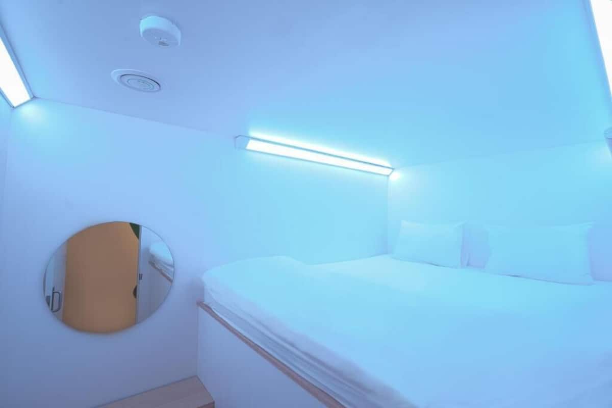 A hotel room with a bed, a round mirror, and a ceiling light fixture.